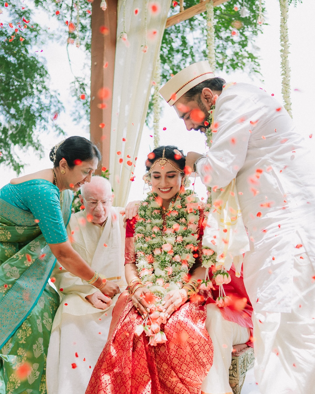 A bride smiling as family shower her with flower petals